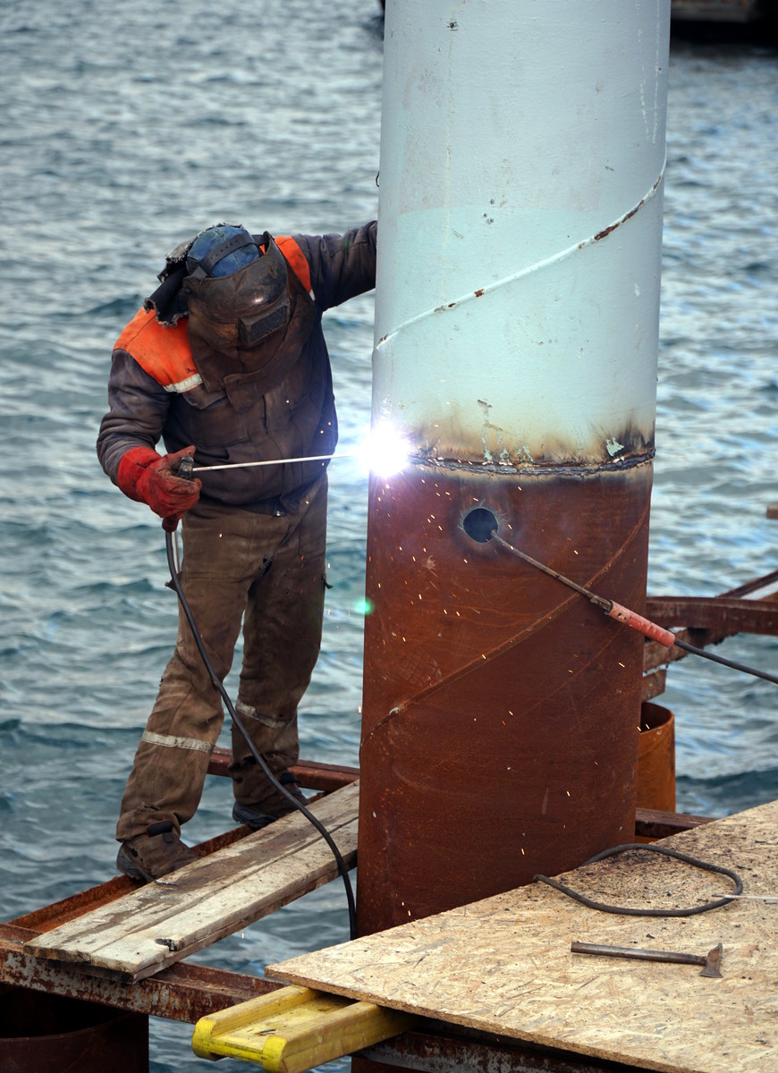 Offshore welder performing structural repair on an oil platform leg over open water